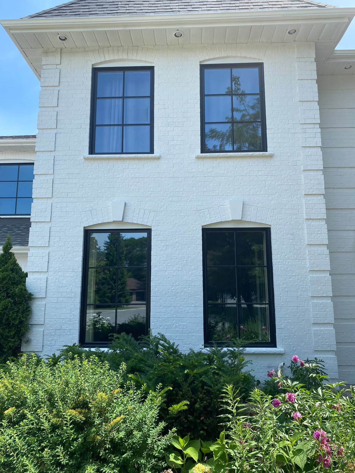 A white brick house with modern, black-framed replacement windows, highlighting a clean, weather-tight professional installation.