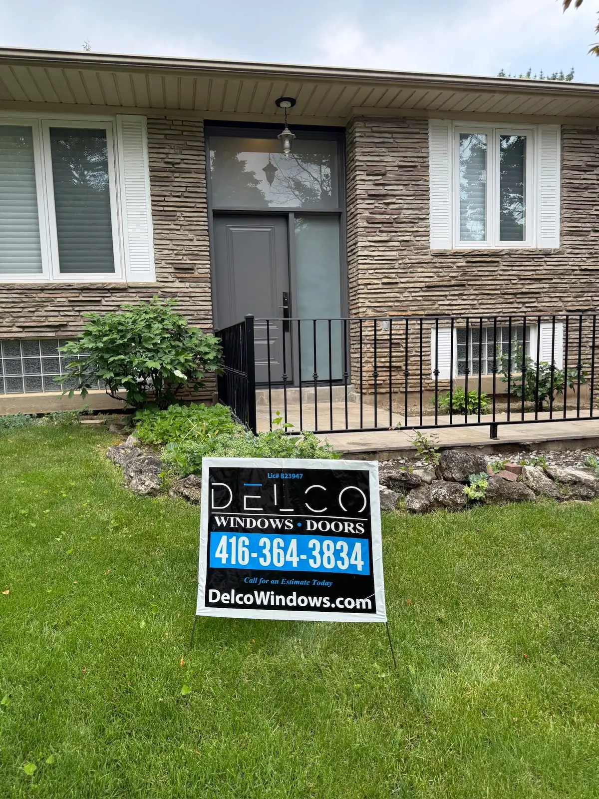 Brick and stone bungalow with a new grey glass entry door and a Delco Windows and Doors lawn sign, door replacement in Vaughan