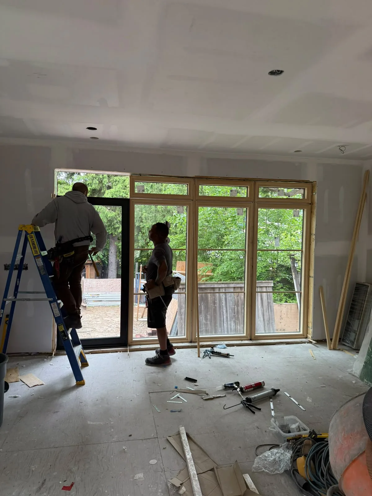 Two installers on ladders fitting a large wall of new windows on a construction site, wholesale window supplier for contractors in Toronto
