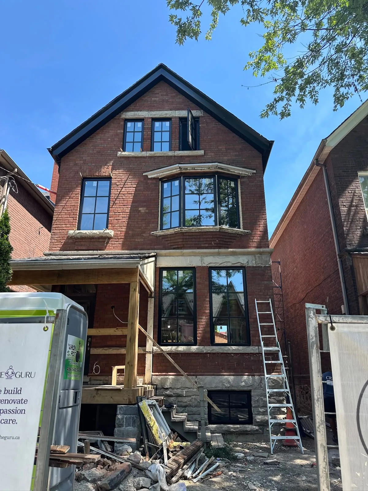 Red-brick Toronto semi under renovation with new black windows and window supply pallets out front, window supplier and PVC windows supplier in Toronto