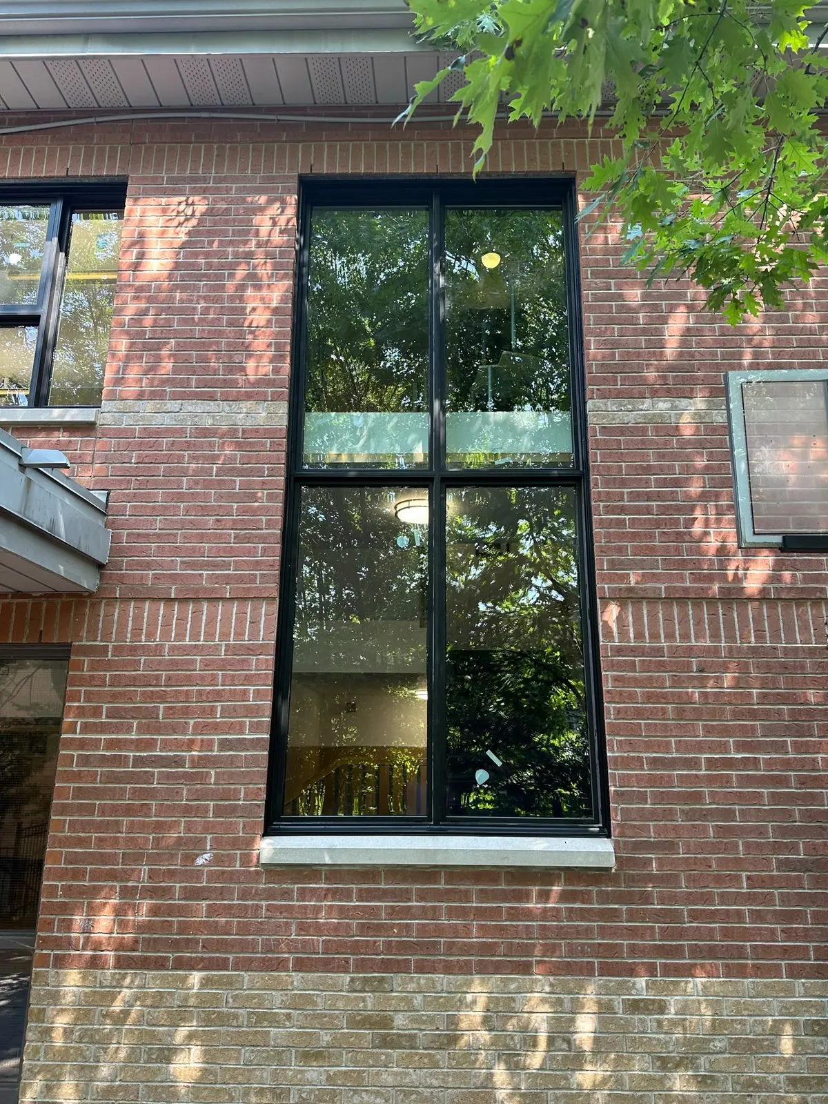 Tall black-frame window with an upper operable section in a red-brick wall, awning window installation in Vaughan