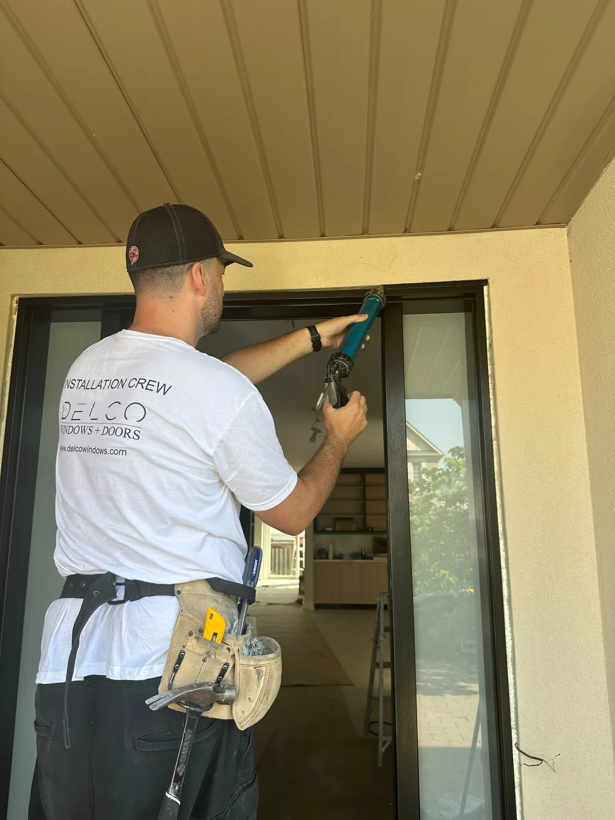 Delco installer in a crew shirt and tool belt sealing a new entry door frame with a caulking gun, door installation in Toronto