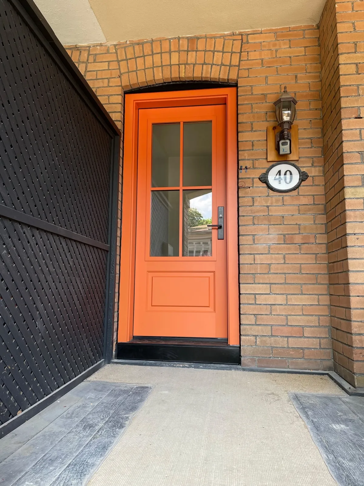 Orange entry door with four glass lites in an arched red-brick entrance, door supplier in Toronto