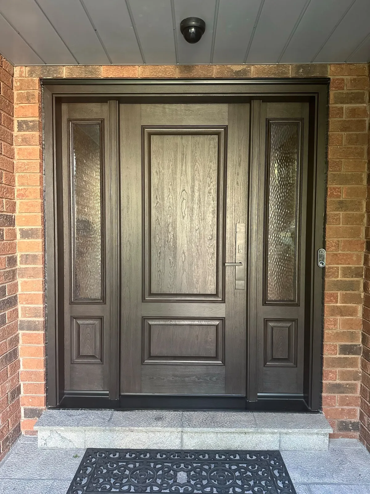 Dark brown woodgrain entry door with two decorative glass sidelites in a red-brick entrance, front door replacement in Toronto