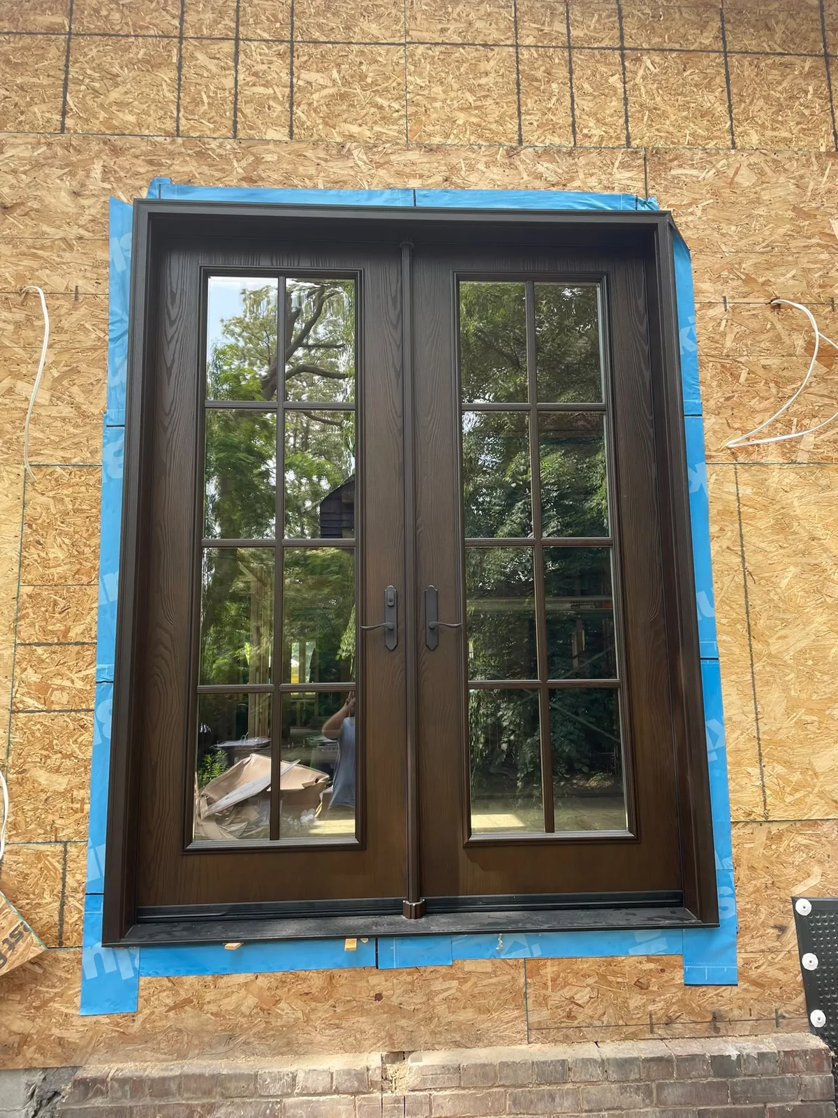 Dark French-style double garden doors with colonial grilles being installed in new wall sheathing, garden door installation in Toronto