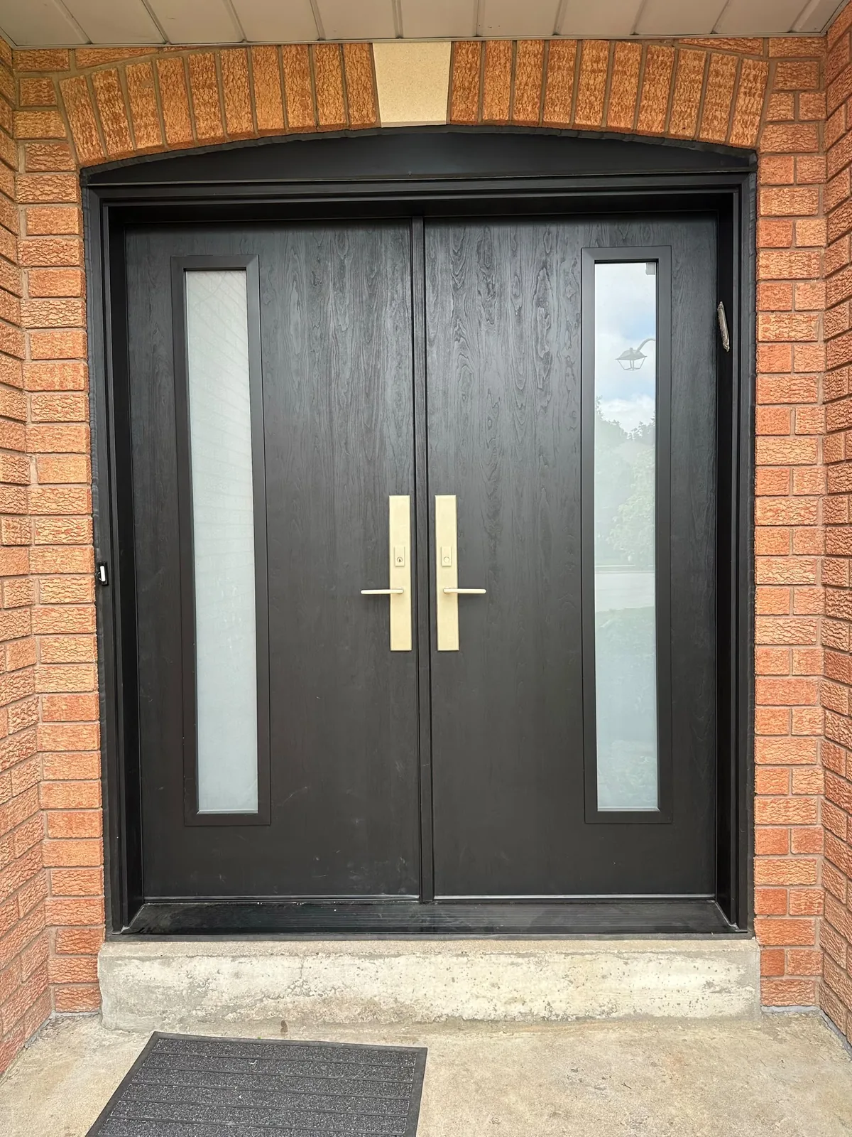 Black double entry doors with tall frosted glass inserts in an arched brick opening, steel entry doors in Toronto