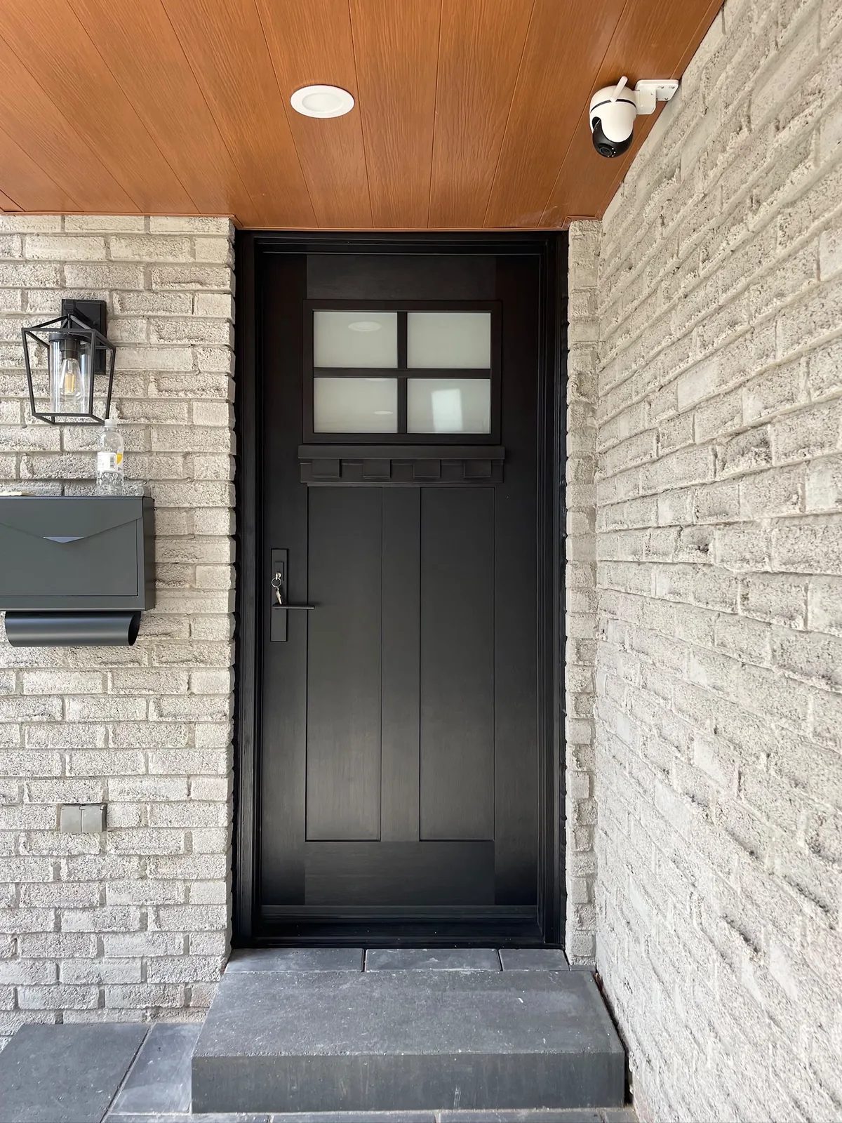 Black craftsman-style entry door with a four-lite window in a grey stone entrance, steel entry doors in Toronto