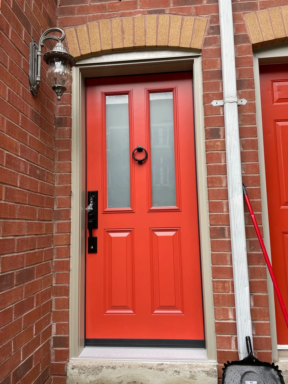 Red entry door with two frosted glass lites in a red-brick townhouse entrance, storm door installation in Toronto