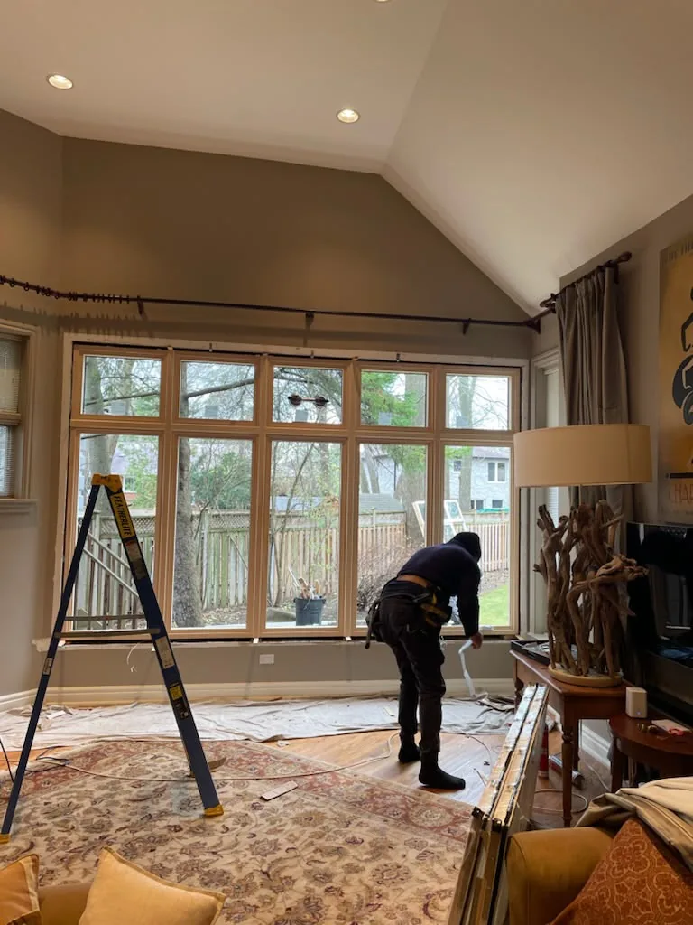 Delco installer on a ladder fitting a large wall of new windows inside a vaulted living room, tilt and turn window installation in Vaughan